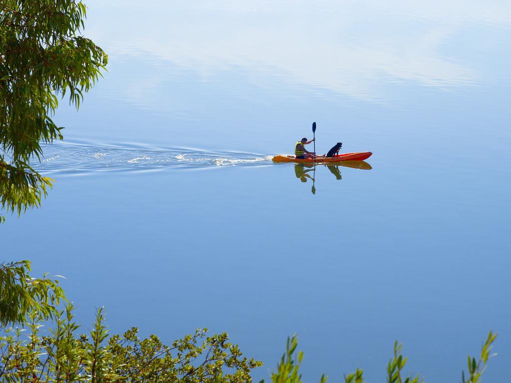Ap Lago Montargil - Conference & Spa מראה חיצוני תמונה The photo shows a serene scene of a person kayaking on a calm body of water. The surface of the water is very smooth, reflecting the surroundings, and there is a gentle wake behind the kayak indicating movement. The kayaker is wearing a life jacket a