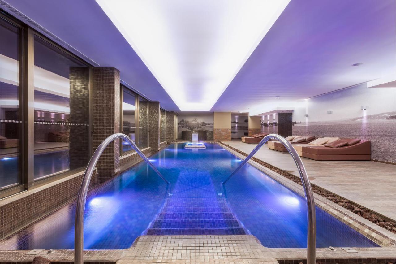 Ap Lago Montargil - Conference & Spa מראה חיצוני תמונה The photo shows a modern indoor swimming pool area. The pool features a sleek design with steps leading into the water and a gentle curve at the sides. The water is illuminated in a blue hue, enhancing the relaxing atmosphere. Surrounding the pool ar