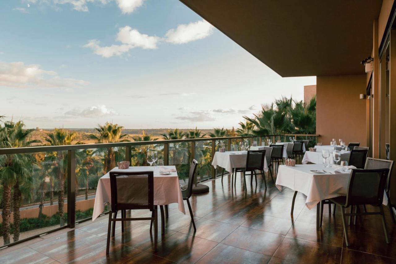 Ap Lago Montargil - Conference & Spa מראה חיצוני תמונה The photo shows a dining area on a balcony with a view. There are several tables set for dining, each covered with white tablecloths. The chairs are wooden and have a simple design. In the background, there are palm trees and a scenic view of the lan