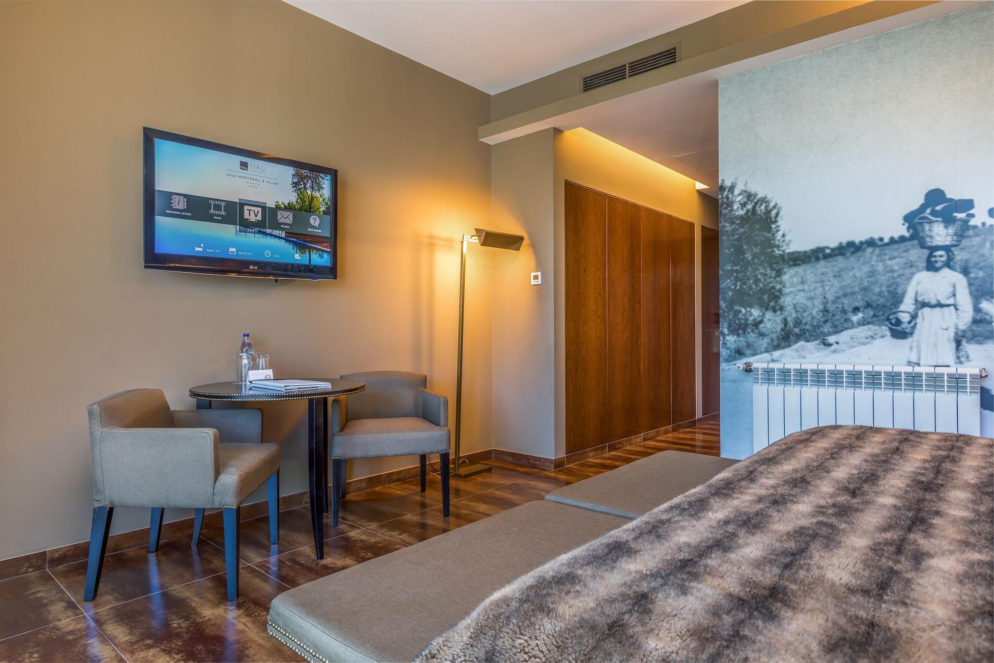 Ap Lago Montargil - Conference & Spa מראה חיצוני תמונה The photo shows an interior of a room, likely a hotel or a modern living space. In the foreground, there is a bed with a textured brown blanket. To one side, there are two comfortable chairs and a small table, possibly with a bottle of water. A flat-