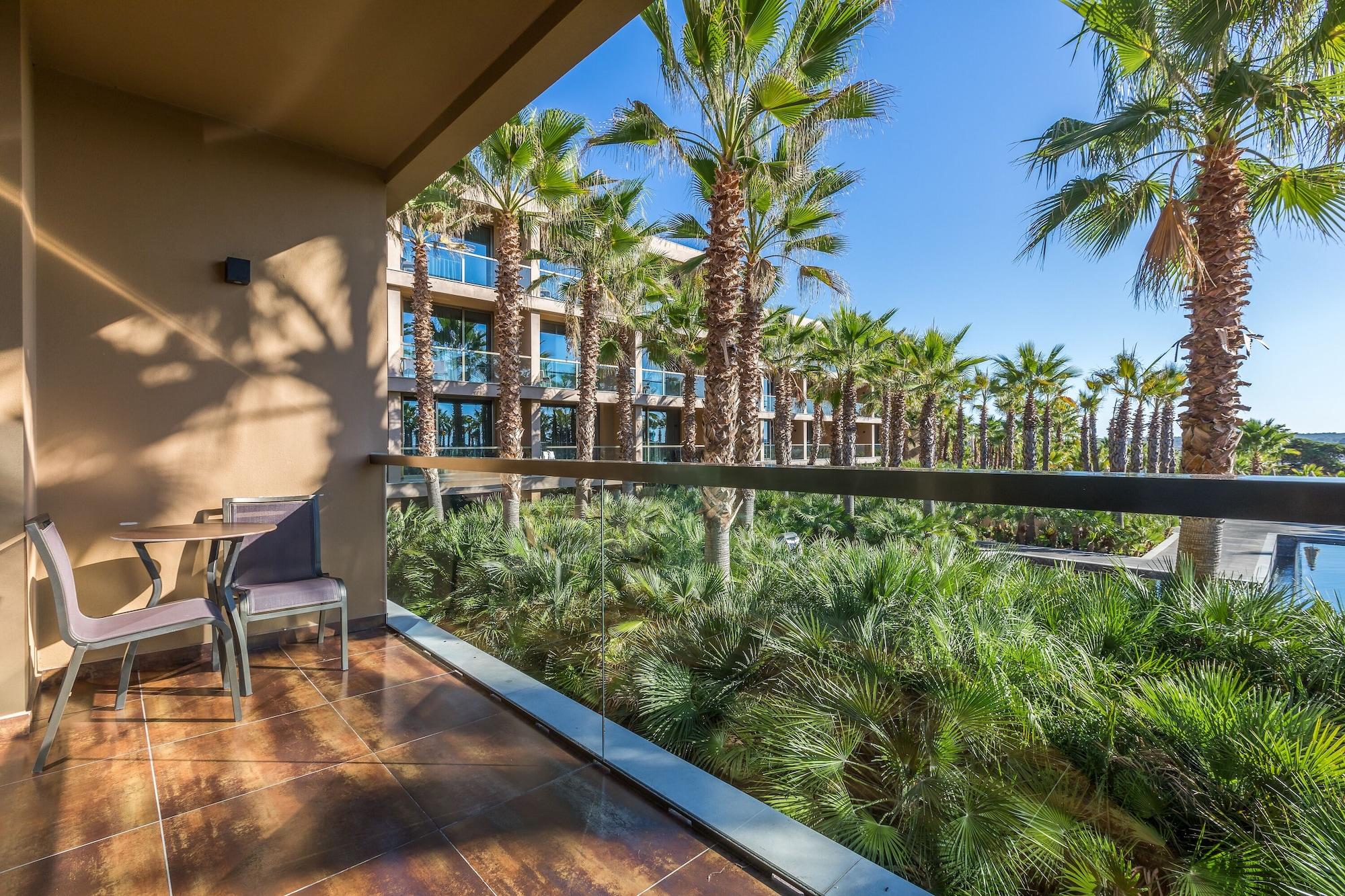 Ap Lago Montargil - Conference & Spa מראה חיצוני תמונה The photo shows a balcony with modern furniture, including a chair and a small table. In the background, there are tall palm trees and lush greenery, suggesting a tropical or resort-like setting. The buildings in the distance are likely part of a hot