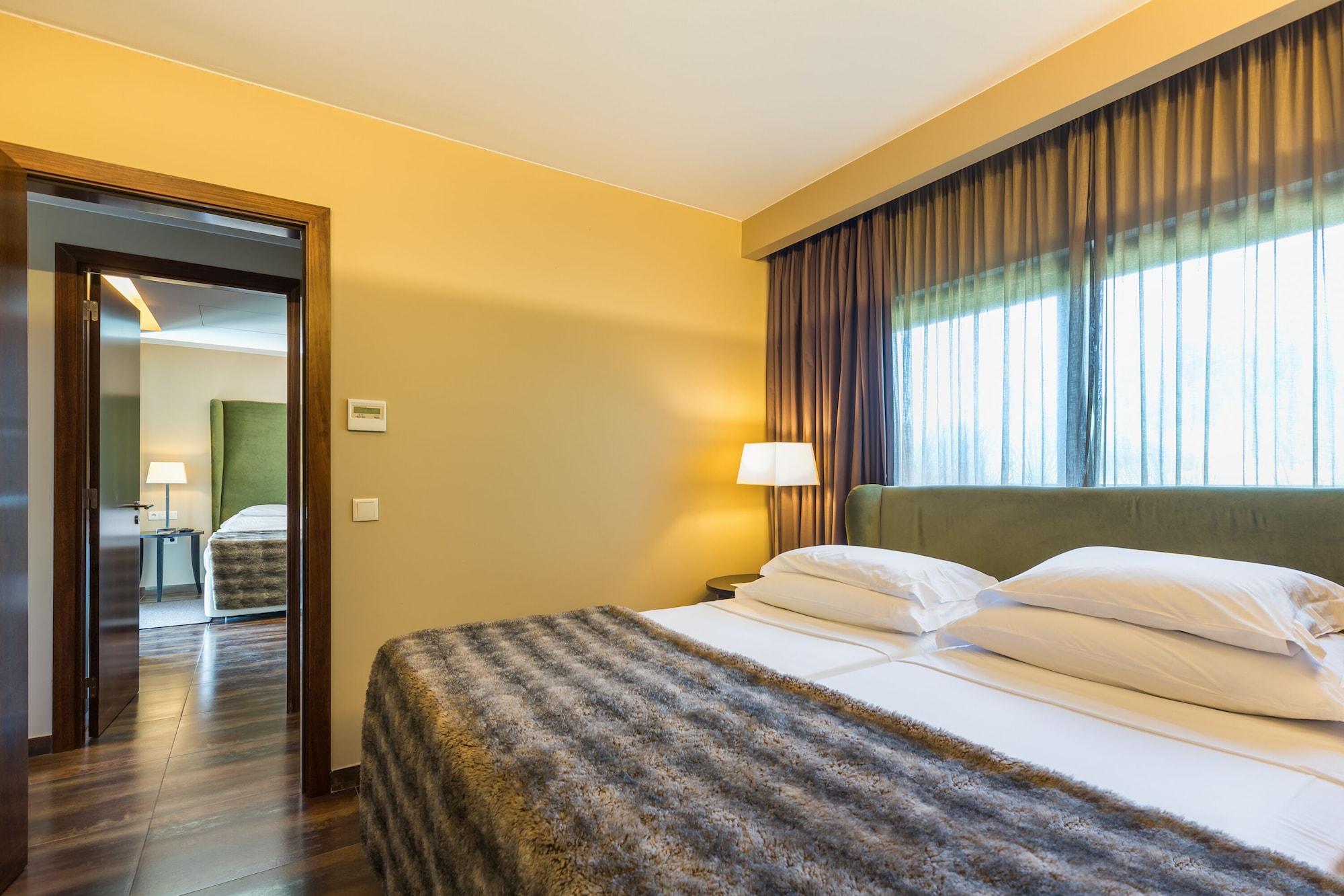 Ap Lago Montargil - Conference & Spa מראה חיצוני תמונה The photo shows the interior of a well-furnished hotel room. It features two beds with white linens and a gray decorative throw on top. The walls are painted a warm yellow, and there are floor-to-ceiling windows covered with dark curtains that allow 