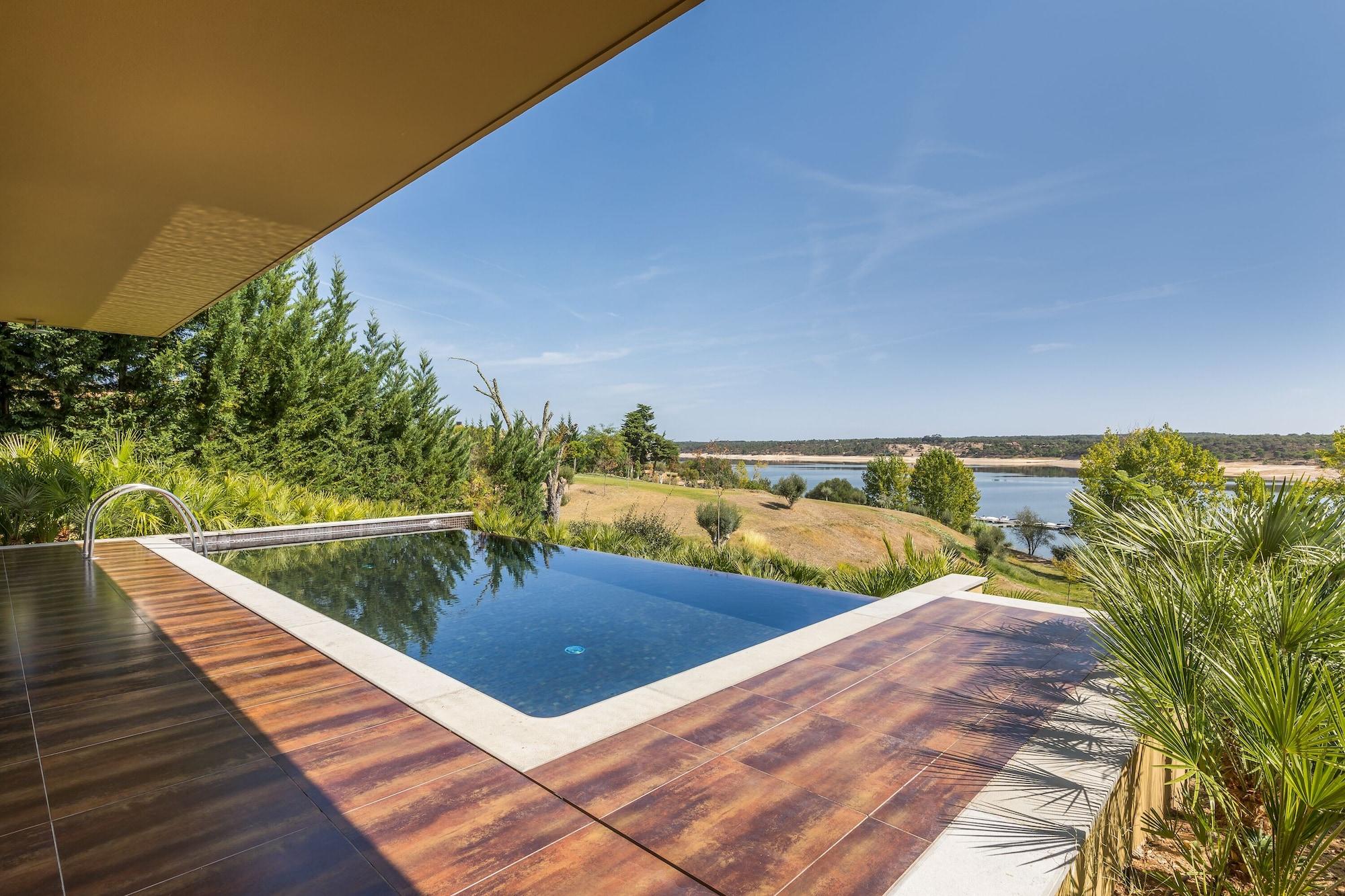 Ap Lago Montargil - Conference & Spa מראה חיצוני תמונה The photo shows a luxurious infinity pool situated on a terrace or deck. The pool features a sleek, modern design with a dark blue surface that reflects the surrounding scenery. In the background, there is a landscape of rolling hills and a body of w