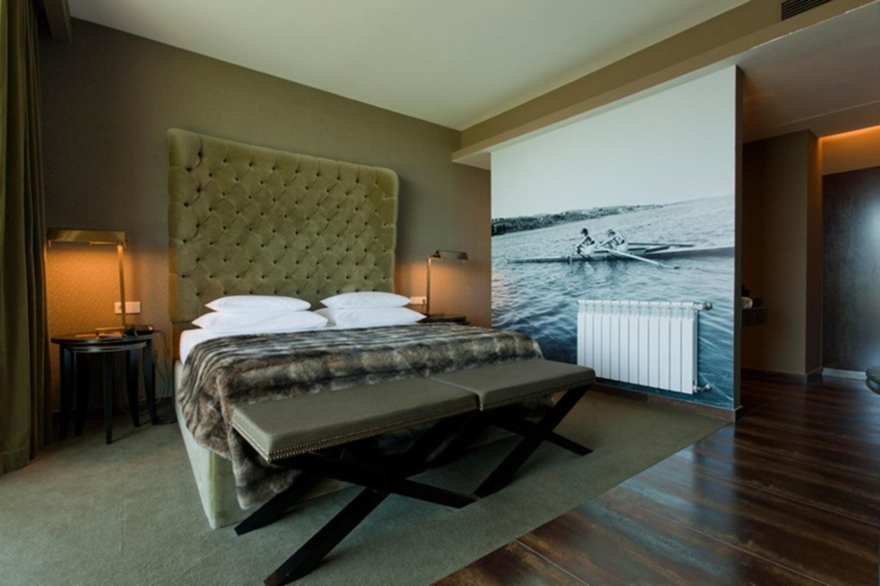 Ap Lago Montargil - Conference & Spa מראה חיצוני תמונה The photo shows a modern hotel room featuring a large bed with a tufted headboard and plush bedding. The color palette is neutral, with shades of green and gray. On one side of the room, there are bedside tables with lamps. A comfortable bench sits a