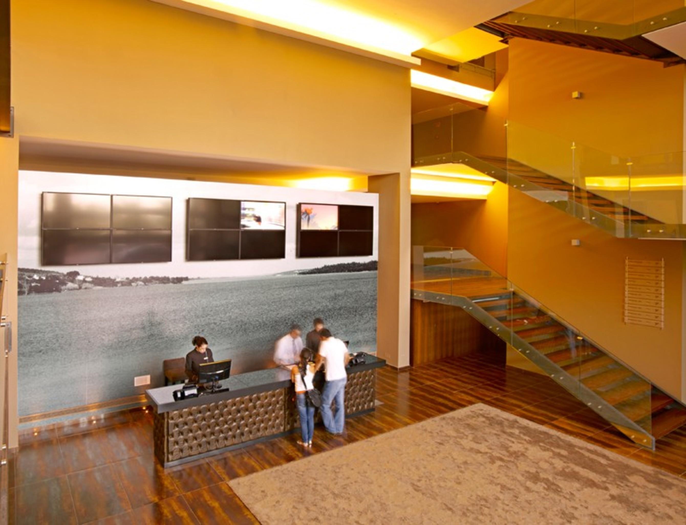 Ap Lago Montargil - Conference & Spa מראה חיצוני תמונה The photo depicts a modern lobby area with a reception desk. The design features a combination of warm colors and wood flooring. In the background, there is a large wall-mounted screen or display, showcasing several monitors. The wall behind the desk