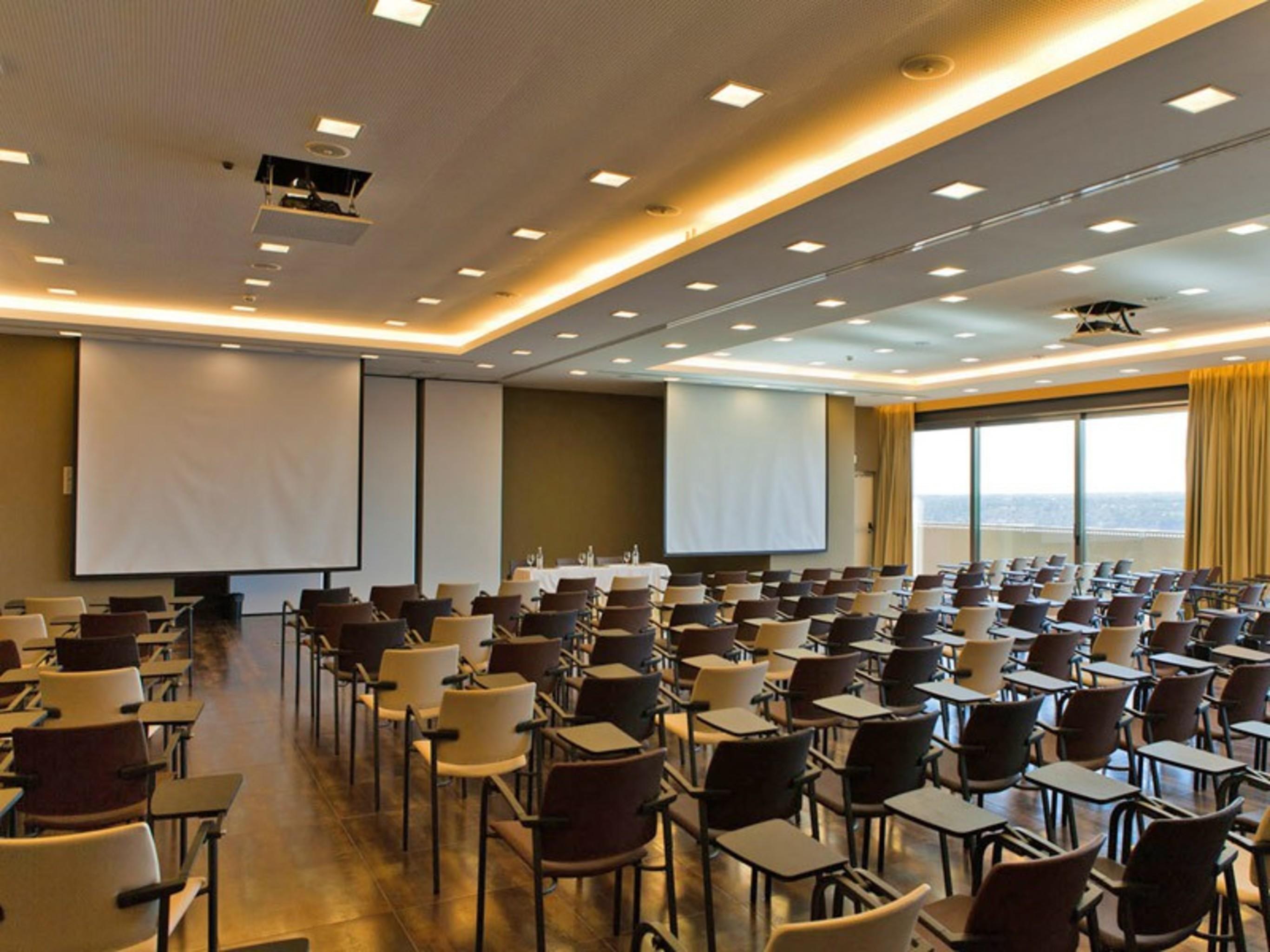 Ap Lago Montargil - Conference & Spa מראה חיצוני תמונה The photo shows a large conference room set up for a presentation or meeting. There are multiple rows of chairs arranged in a semi-theater style, facing two large projection screens. The room has a modern design, with soft lighting and large windows 