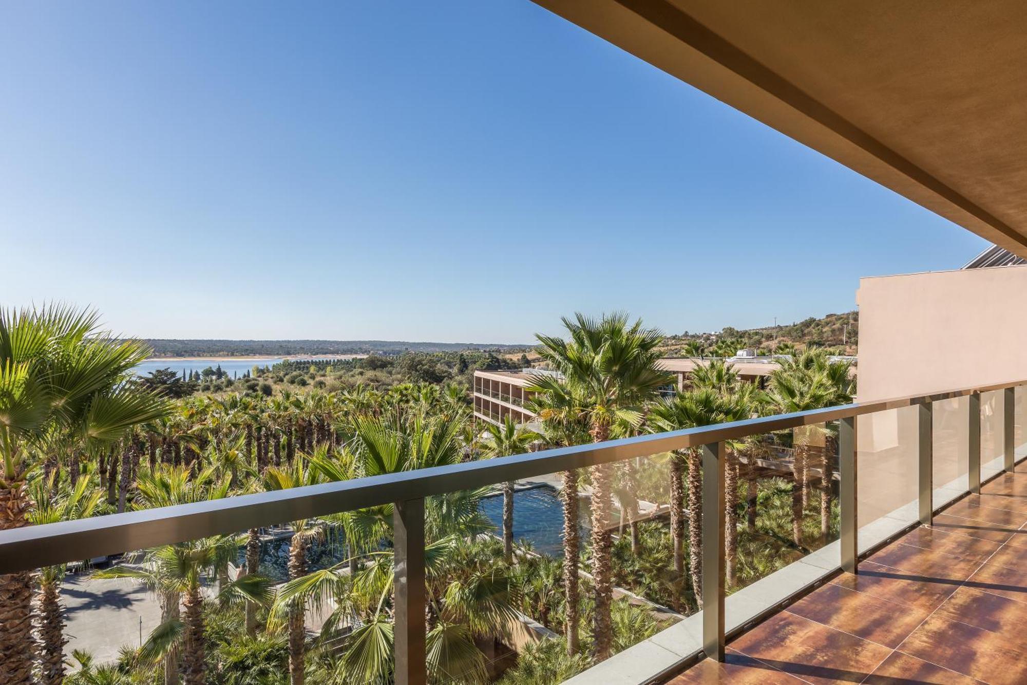 Ap Lago Montargil - Conference & Spa מראה חיצוני תמונה The photo shows a scenic view from a balcony overlooking a lush landscape with palm trees. In the distance, there seems to be a body of water, possibly the ocean or a lake. The sky is clear and blue, indicating nice weather. The overall atmosphere is