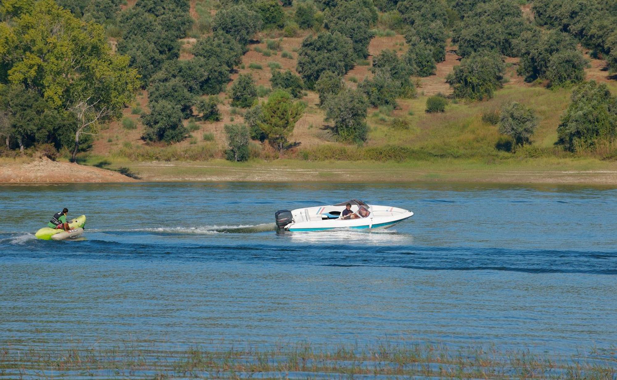 Ap Lago Montargil - Conference & Spa מראה חיצוני תמונה The photo shows a scene on a water body, likely a river or lake. In the foreground, a speedboat is moving quickly through the water, leaving a wake behind it. There are two people visible in the boat. In the background, there is a hilly area covered 