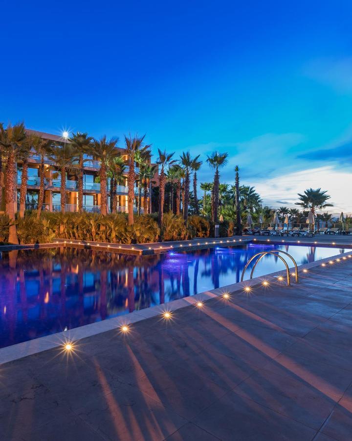Ap Lago Montargil - Conference & Spa מראה חיצוני תמונה The image shows a serene and inviting outdoor area with a large swimming pool that features a beautiful blue hue, likely illuminated by lights. Surrounding the pool are well-maintained palm trees and lush greenery, creating a tropical atmosphere. In 